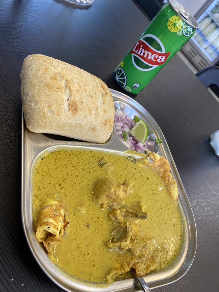 Chicken curry in a steel dish with a bread roll